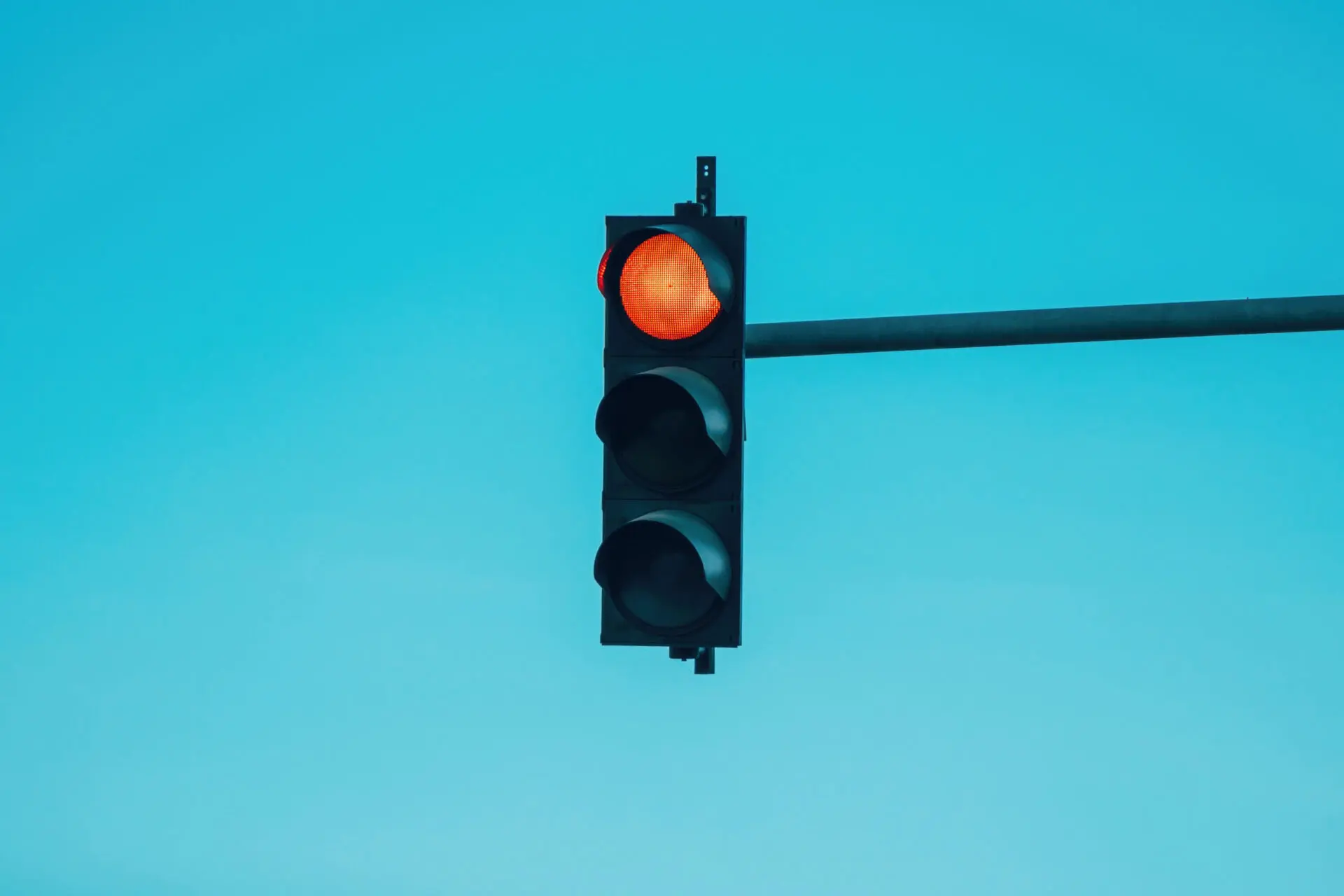 Red traffic light surrounded by blue sky
