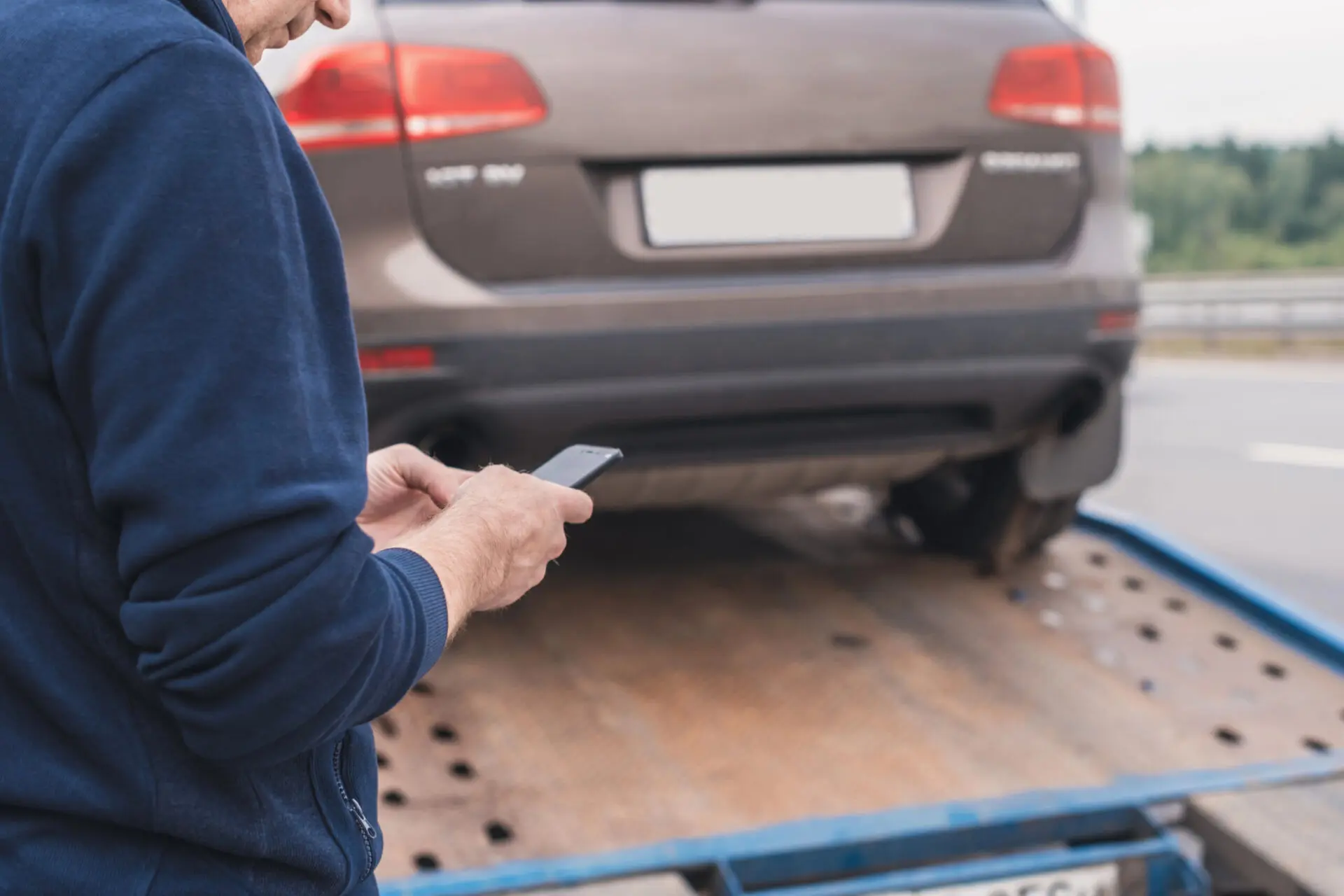 Man texting on phone while car getting towed