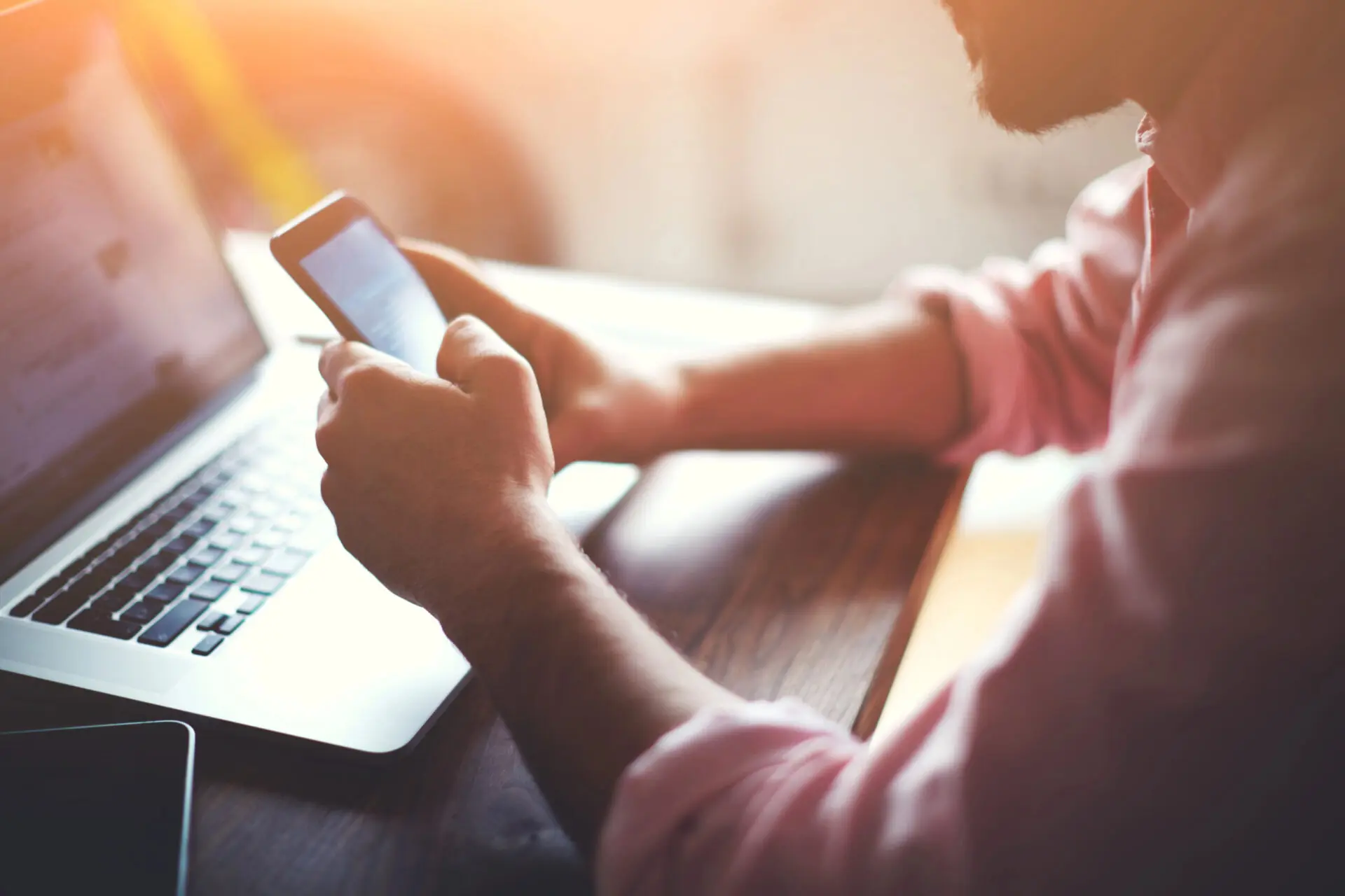 Man using smartphone in front of laptop.